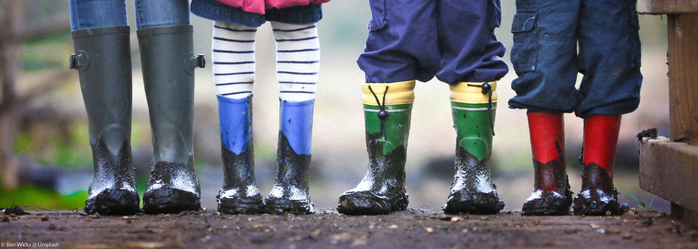 Kinderfüße in bunten Gummistiefeln auf einem matschigen Feldweg