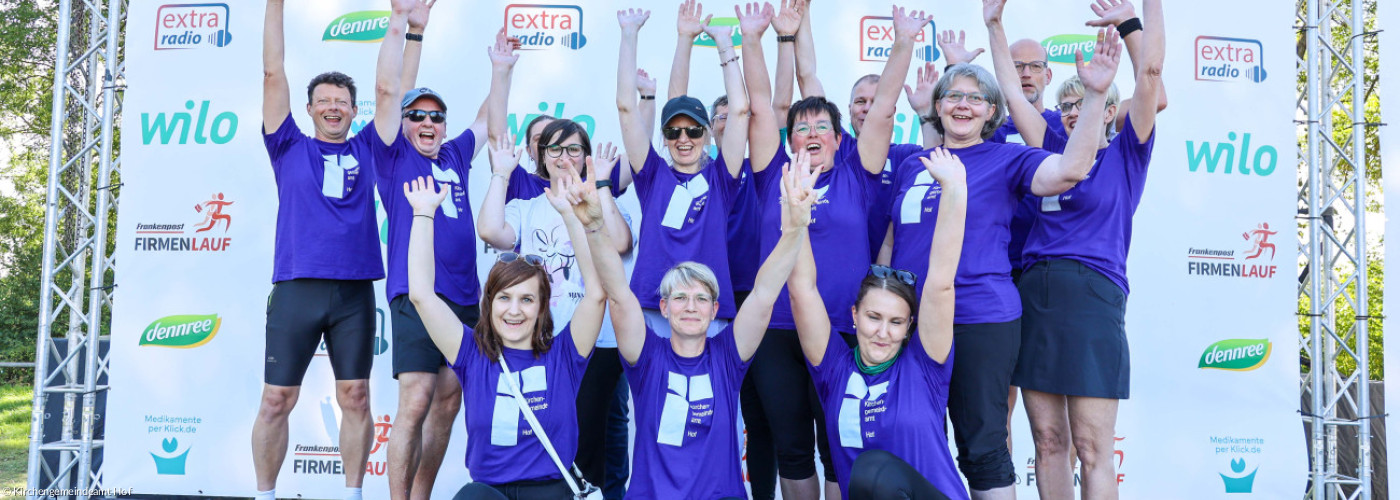 Mitarbeitende des Kirchengemeindeamtes Hof in blauen Trikots beim Firmenlauf reißen die Arme nach oben
