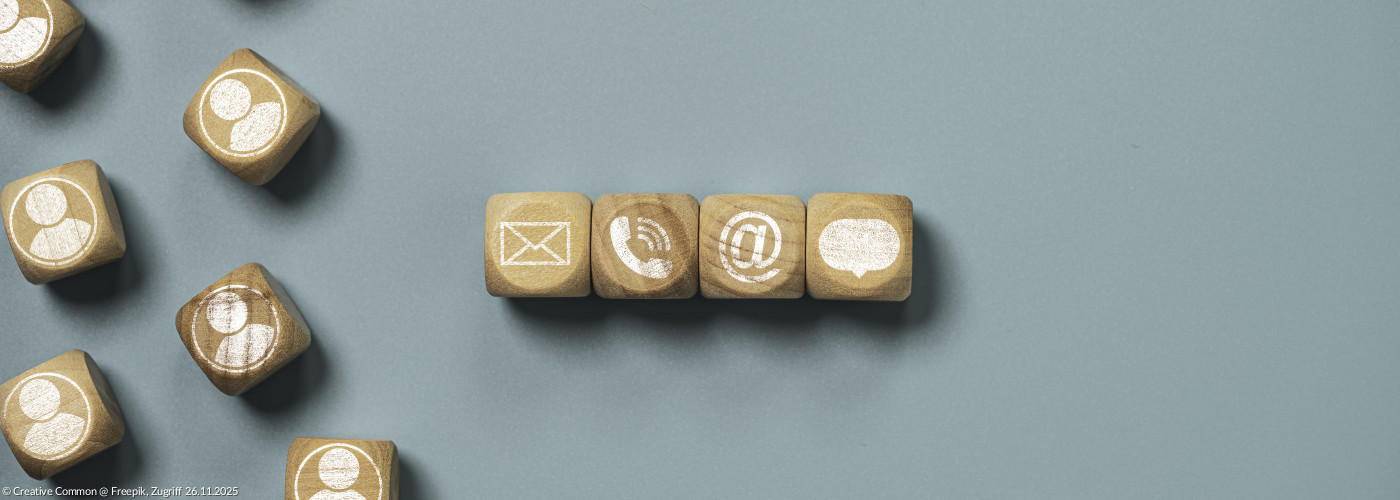 Holzwürfel liegen unsortiert auf einem flachen Hintergrund. Darauf sind Kontakt- und Emailsymbole