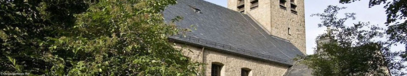 Christuskirche vor Bäumen, grauer Backsteinbau mit Turm
