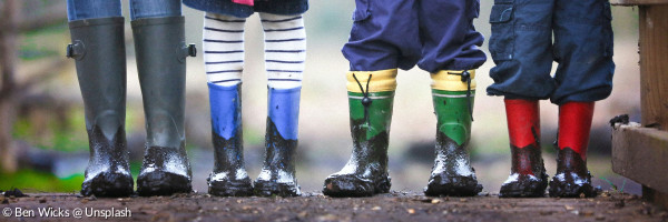Kinderfüße in bunten Gummistiefeln auf einem matschigen Feldweg