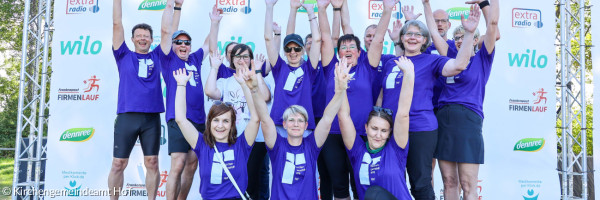 Mitarbeitende des Kirchengemeindeamtes Hof in blauen Trikots beim Firmenlauf reißen die Arme nach oben