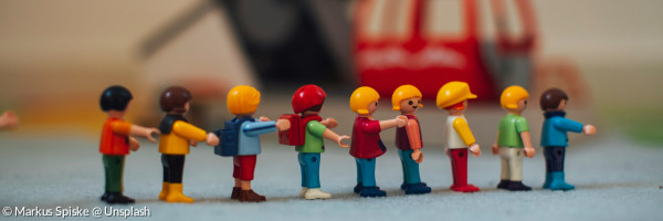 Playmobilmännlein sind in einer Reihe aufgestellt. Im Hintergrund sieht man ein Playmobilfahrzeug